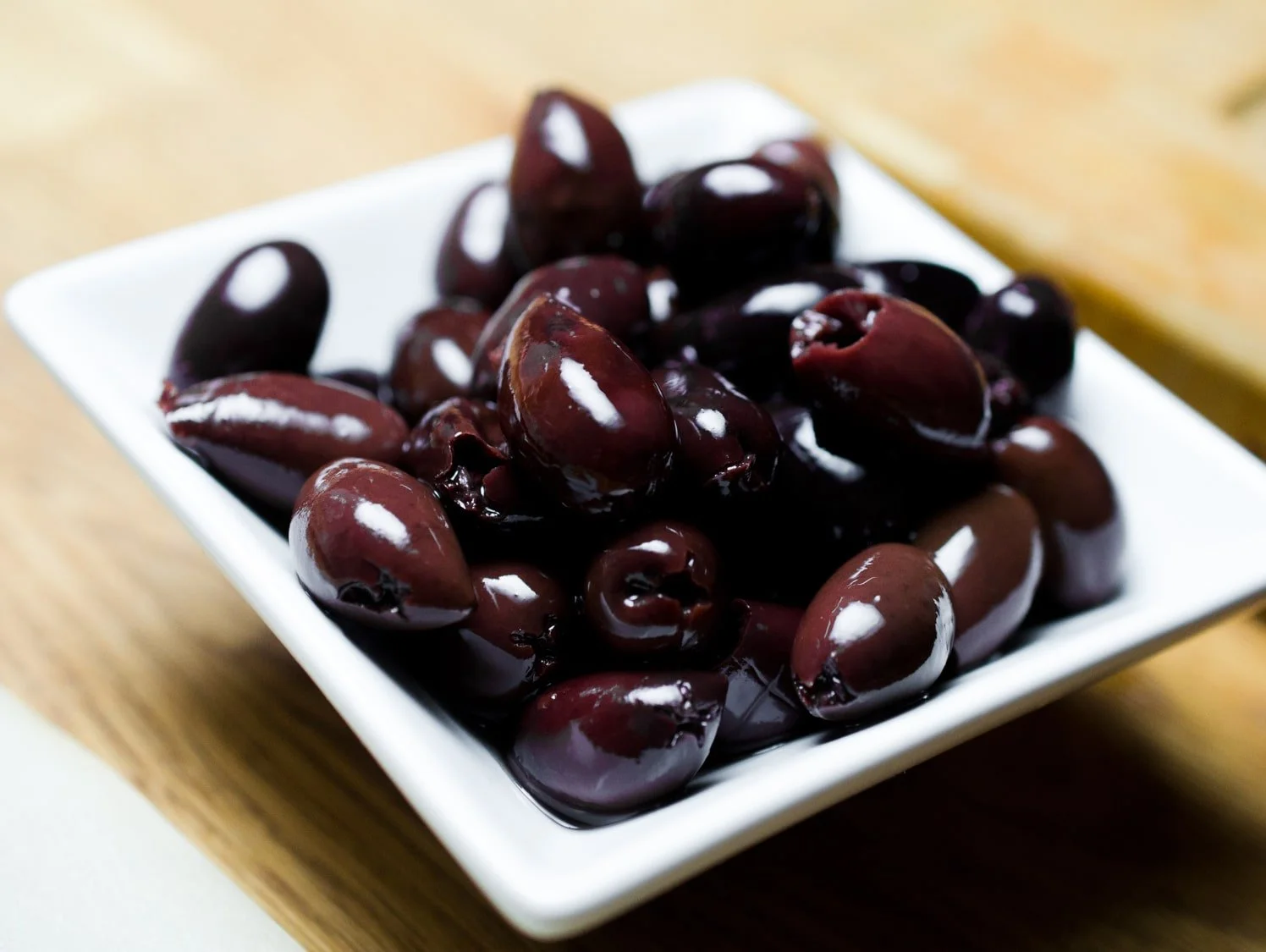 a white dish of juicy black kalamata olives