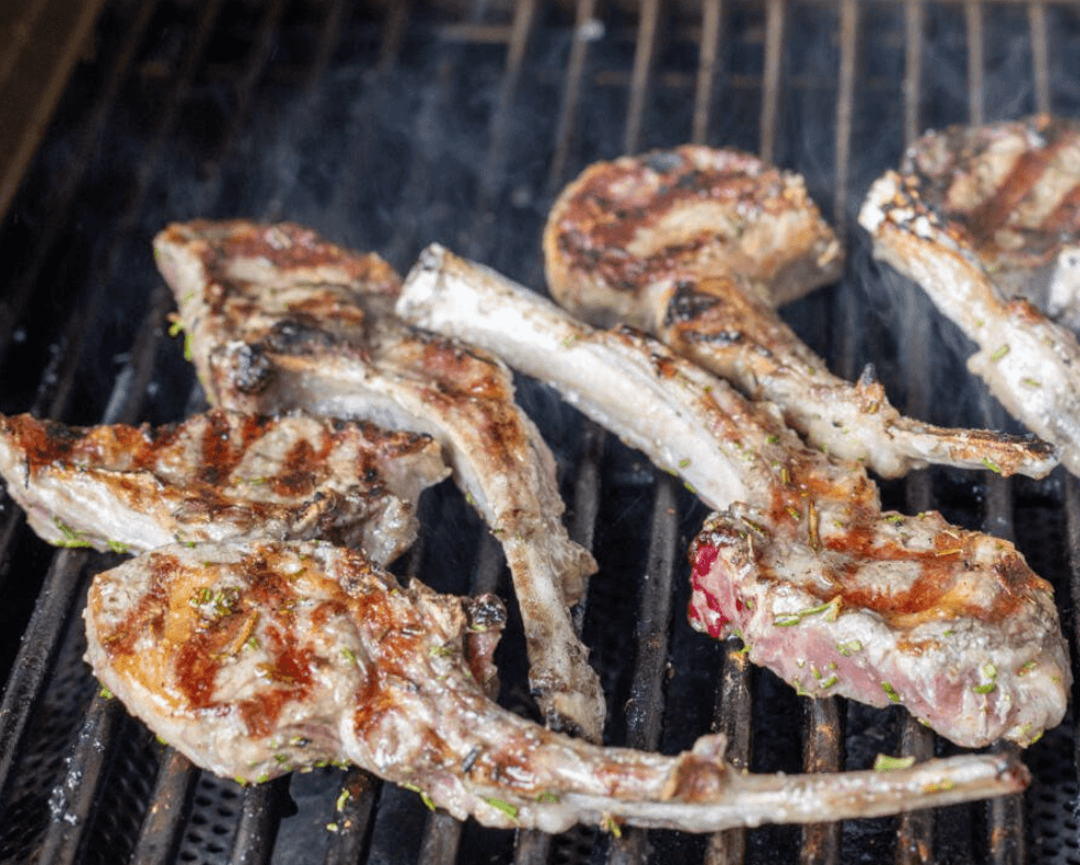 Lamb chops grilling on a barbecue with grill marks and some smoke.