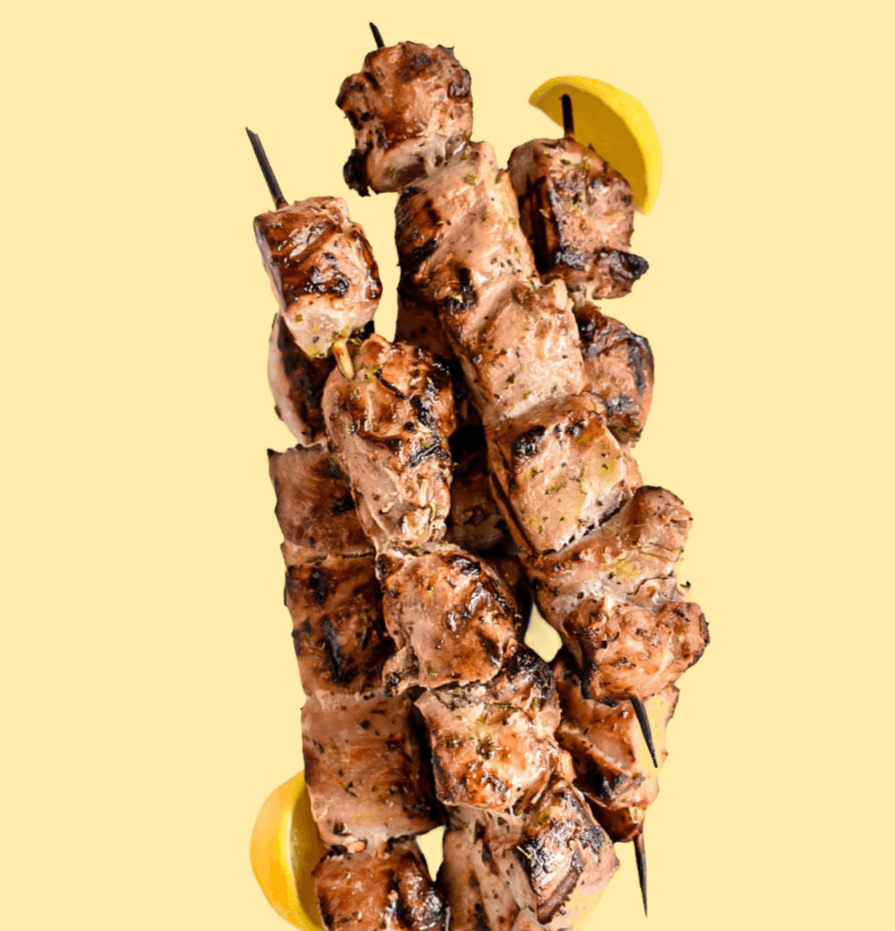 Closeup of souvlakia, skewers of grilled meat, on a light yellow background.