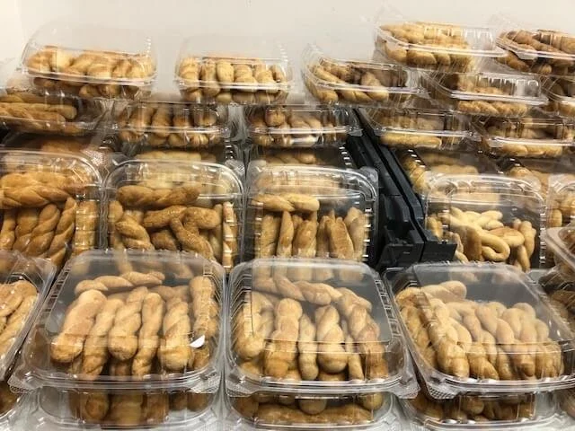 Multiple clear plastic to-go containers filled with Greek koulourakia cookies stacked in a display.