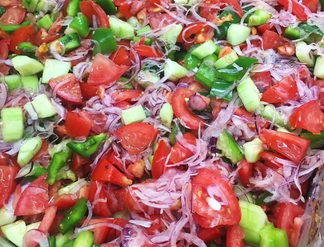 A close-up of a chopped Greek salad with tomatoes, purple onions, green bell peppers, and cucumbers