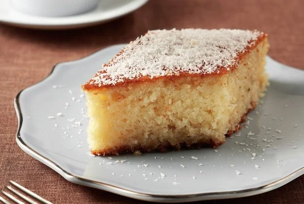 A slice of a Greek coconut cake called indokarido on a white plate with shredded coconut on top