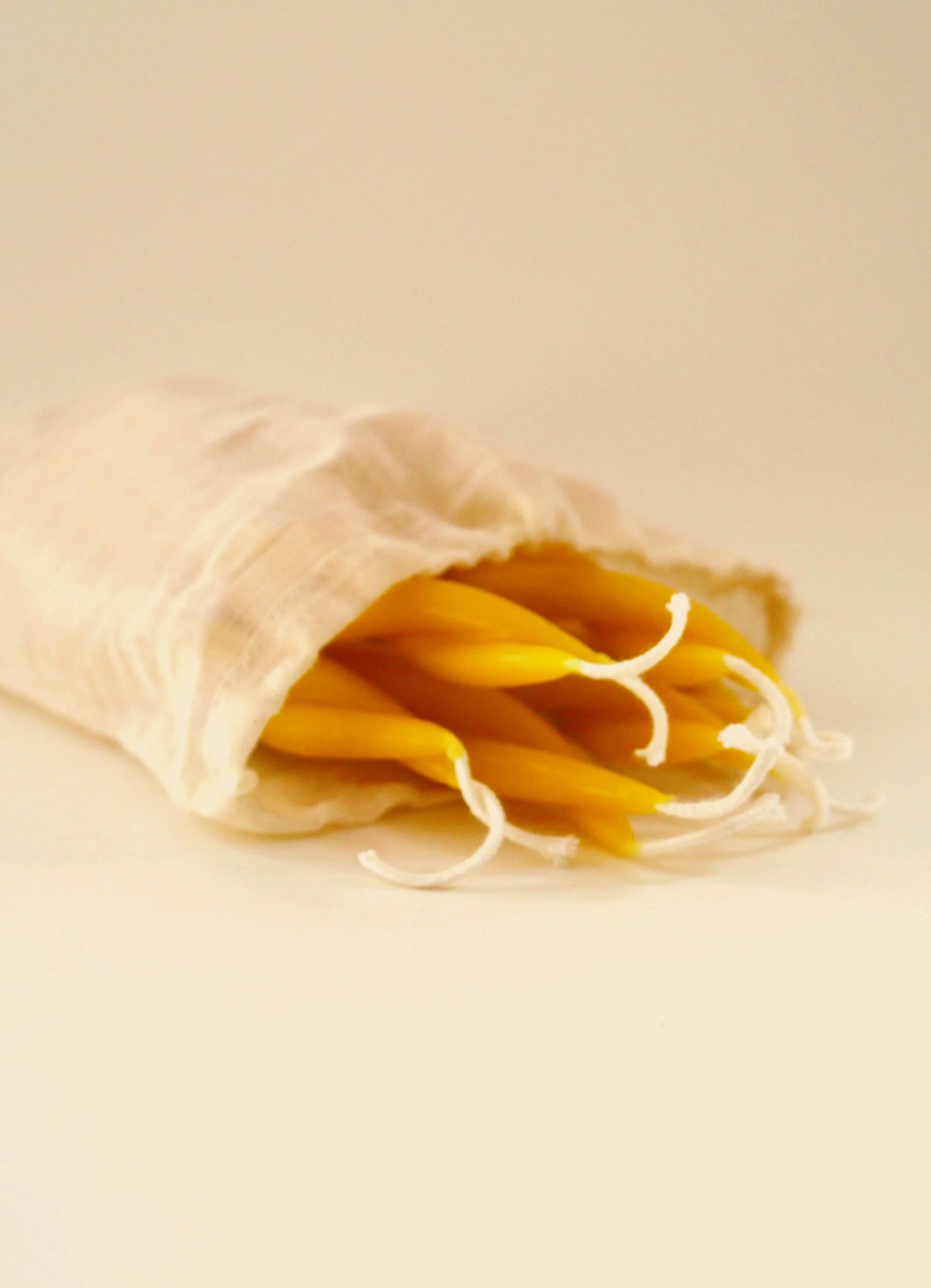 A detail view of twisted beeswax taper candles inside of an eco-friendly muslin cotton pouch. Tapered candlesticks for clean burning unscented natural candlelight.