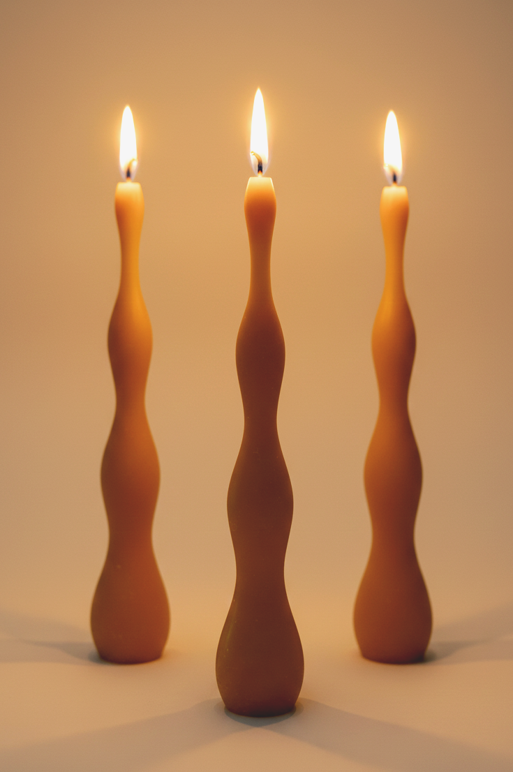 Pure beeswax handmade wavy tapered candlesticks lit in dim setting to showcase their unique silhouette. Unscented clean burning candlelight.