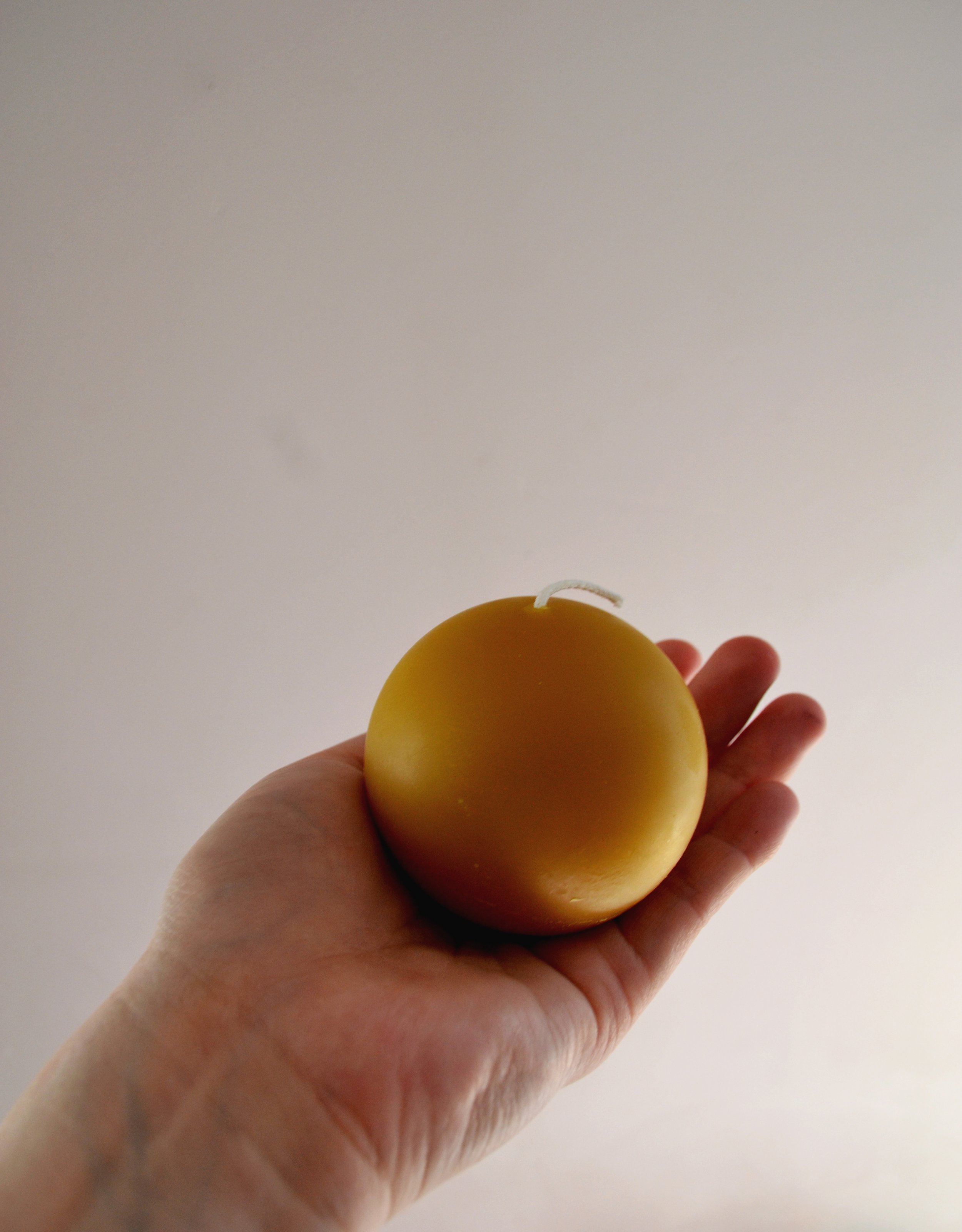 Natural beeswax round ball candle held in hand to show size and scale. Unscented candlelight for evening rituals and natural ambiance.