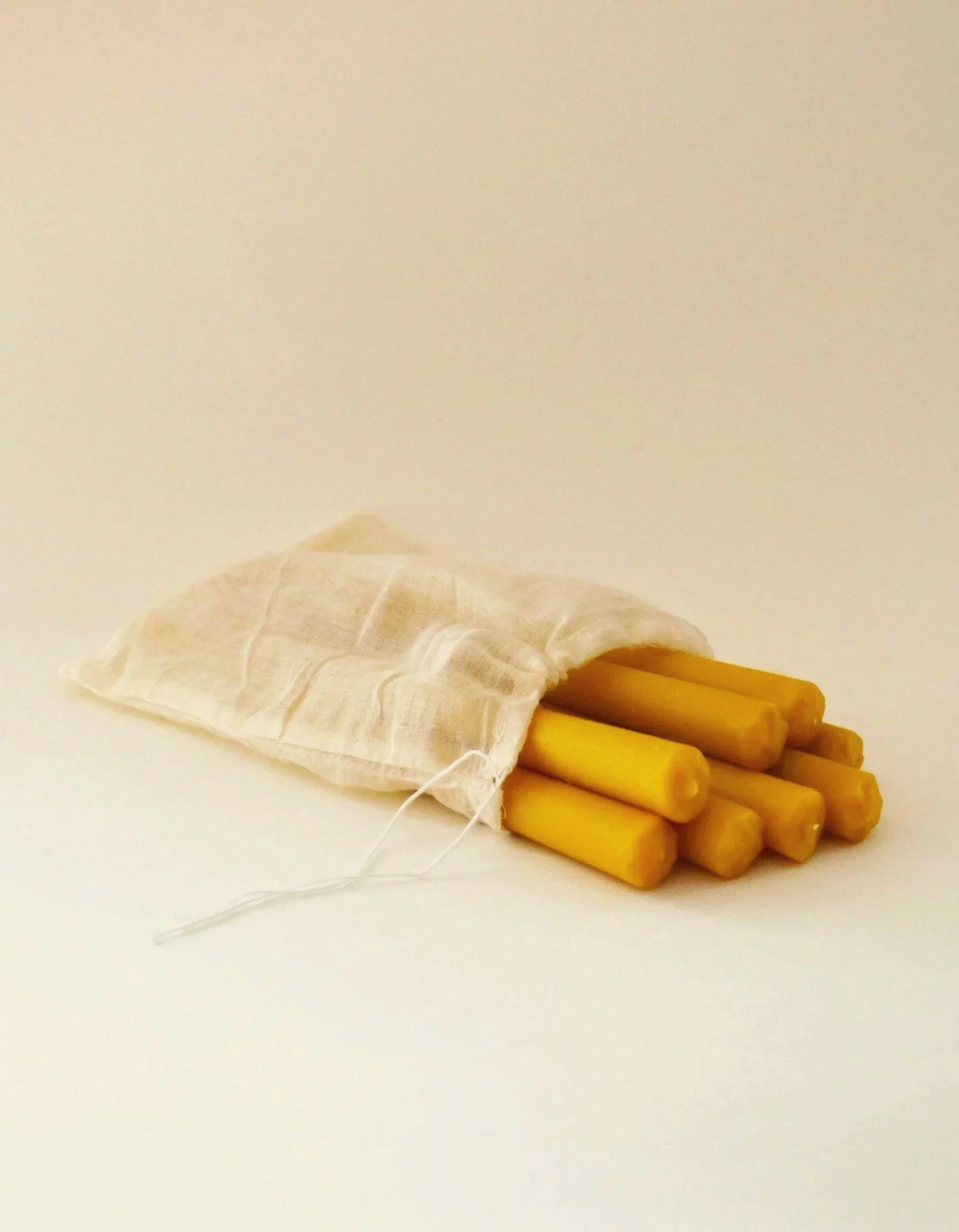 Handmade beeswax taper candles with a soft round tapered shape, in a natural cotton muslin pouch for storage.