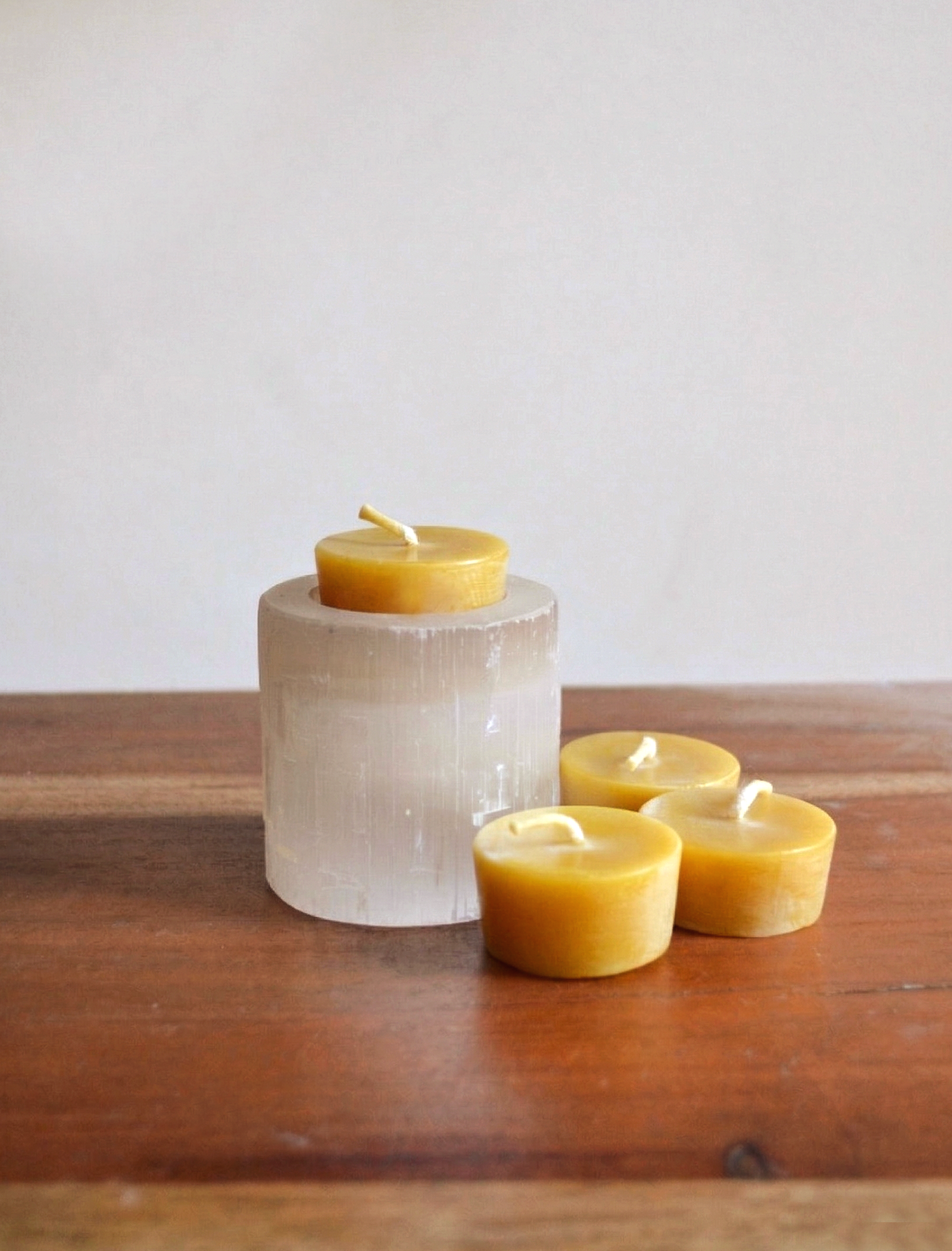 Pure beeswax no waste tea light candles with cotton wicks. One tealight sits in a selenite candle holder with three beside it. Natural zero waste tealights.
