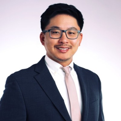 Professional portrait of a man with glasses, wearing a suit and tie, smiling against a plain background.