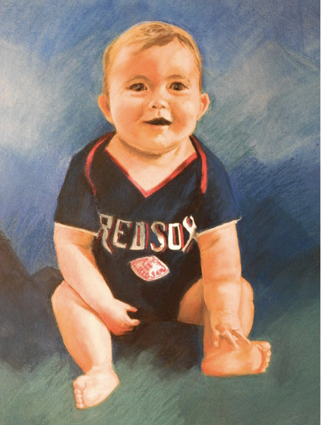 A young child with blond hair and chubby cheeks, sitting on a multicolored surface, wearing a black Boston Red Sox T-shirt with red accents. The child is smiling and looking directly at the camera.