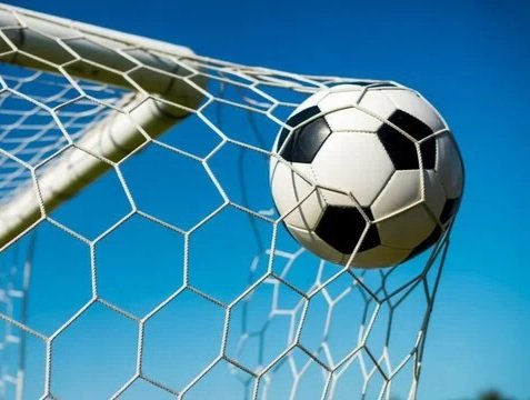 A soccer ball in the goal net with a blue sky background.