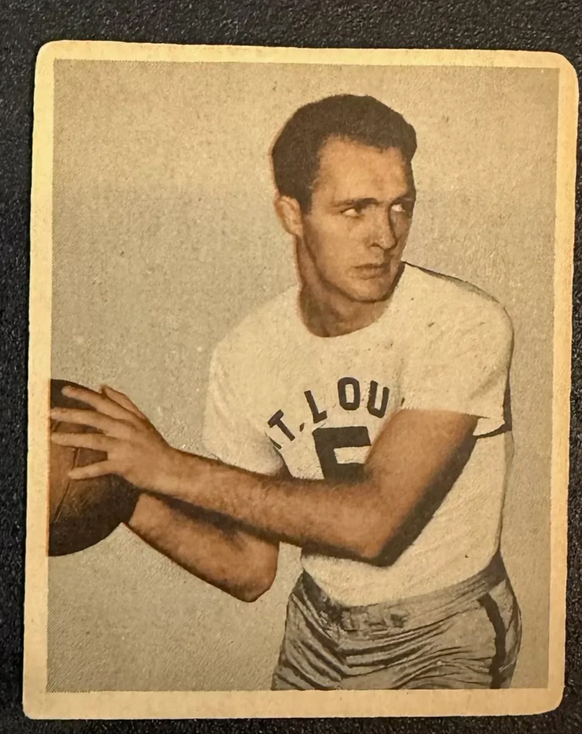 Black and white vintage photo of a young male athlete in a T. LOU T-shirt holding a basketball, with another person's arm partially visible.