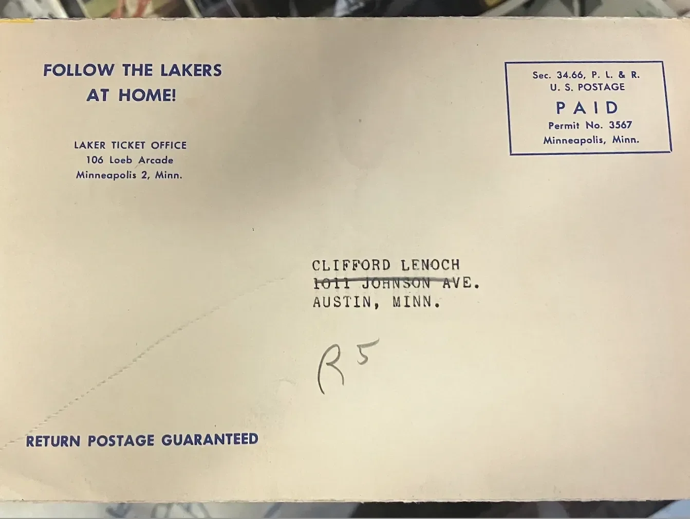 A vintage-style envelope addressed to Clifford Lenoch in Austin, Minnesota, with a return address from the Lakers Ticket Office in Minneapolis, Minnesota. The envelope shows a stamp indicating it has been paid and postage has been guaranteed.