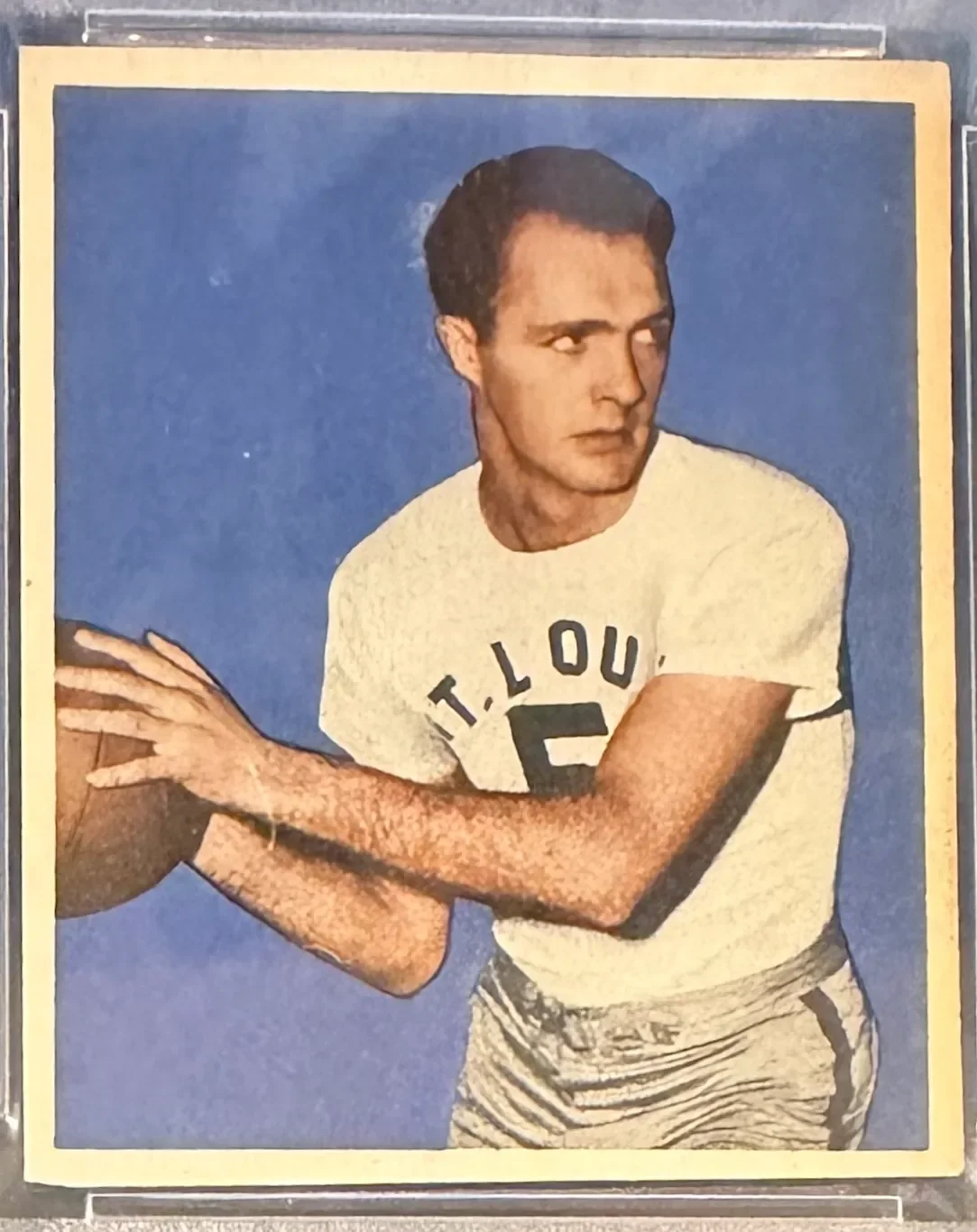 A young man in a white T-shirt holding a basketball, looking to the side against a blue background.