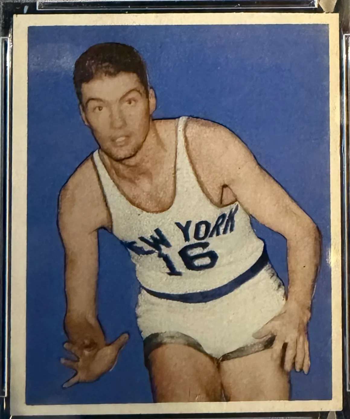 A vintage basketball card featuring a male player in a white jersey with 'New York' and the number 16, posing against a blue background.