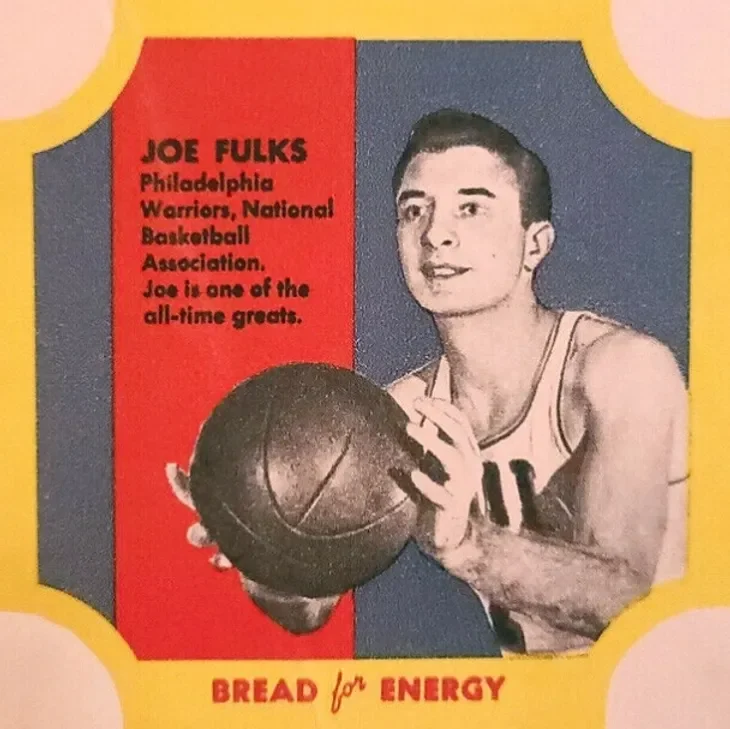 A vintage trading card featuring Joe Fulks, a basketball player for the Philadelphia Warriors, holding a basketball. The card highlights that Joe Fulks is one of the all-time greats and includes a slogan, "BREAD for ENERGY," with a colorful design.