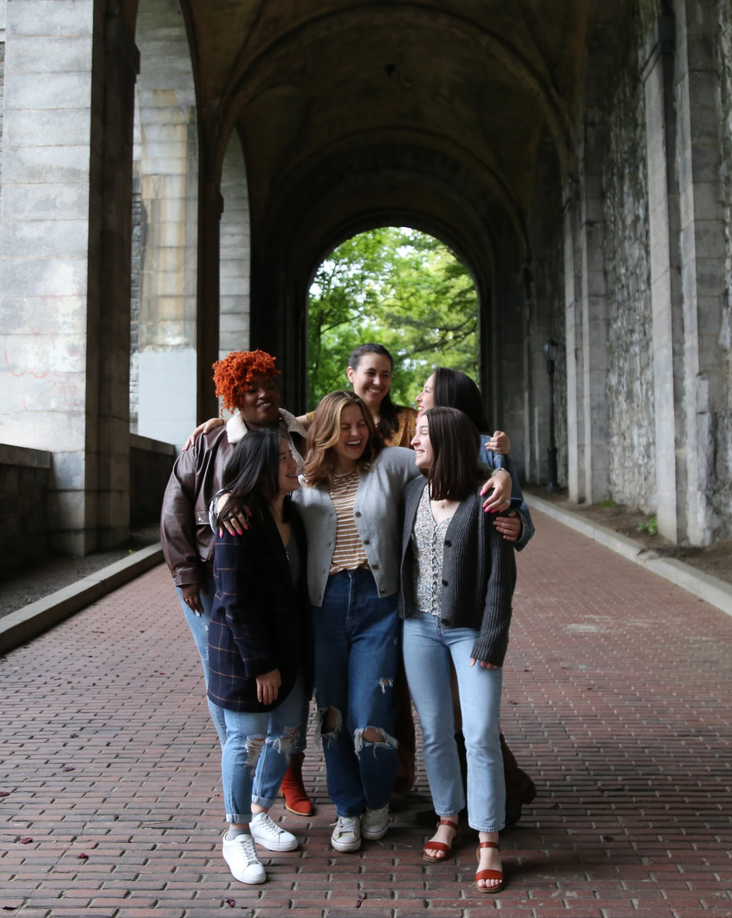 6 women, all part of Mezzo, an a cappella group, standing in a covered archway, arms around each other and laughing