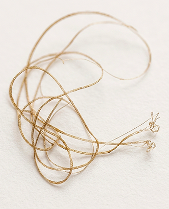 A tangled piece of gold-colored string or thread on a plain white surface.
