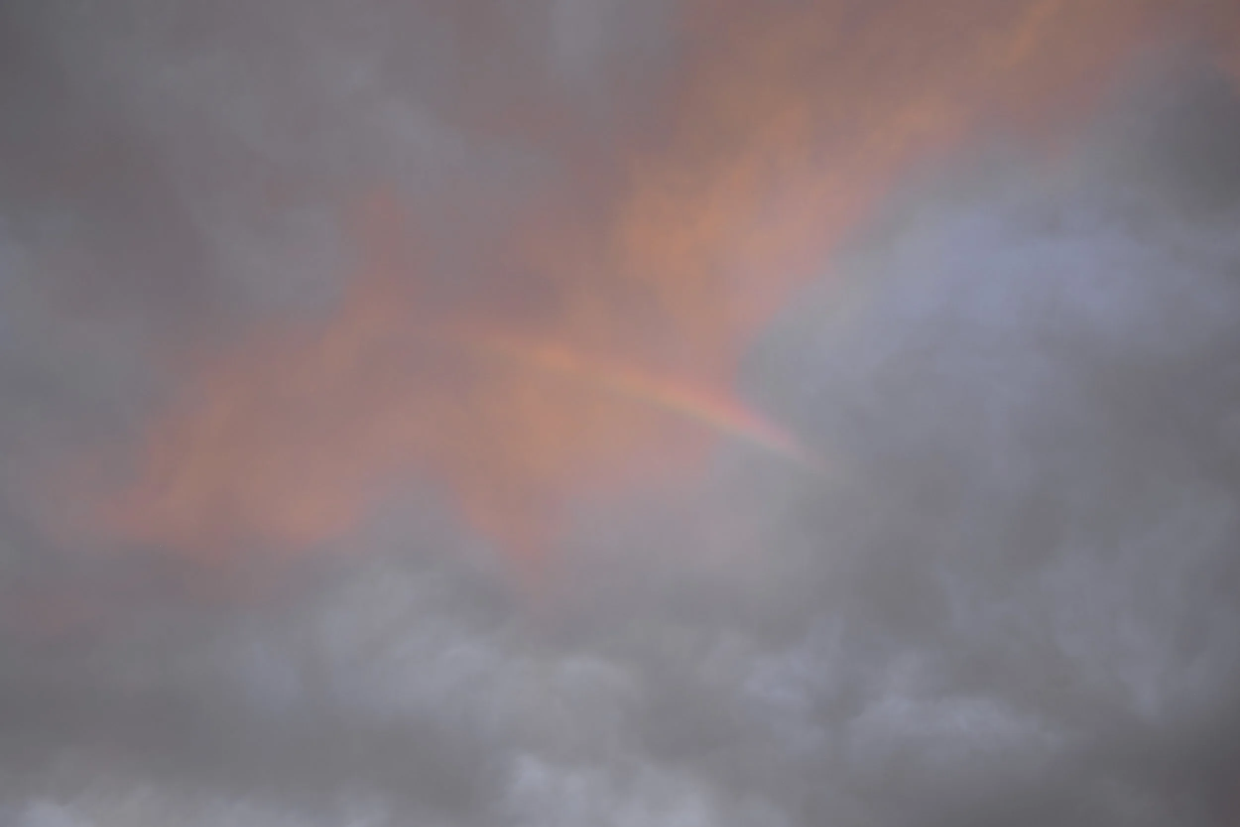 A cloudy sky at sunset or sunrise with a faint rainbow visible in the center.