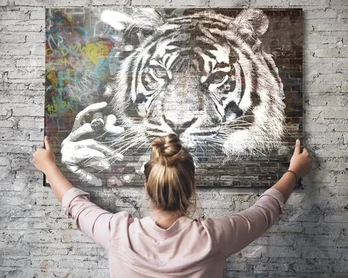 Person with hair in a bun standing with arms outstretched in front of a graffiti mural of a tiger's face on brick wall