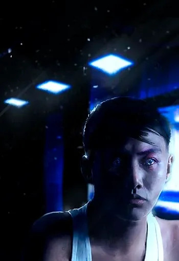 A person with short dark hair looking at the camera in a dark room with blue and white lights.