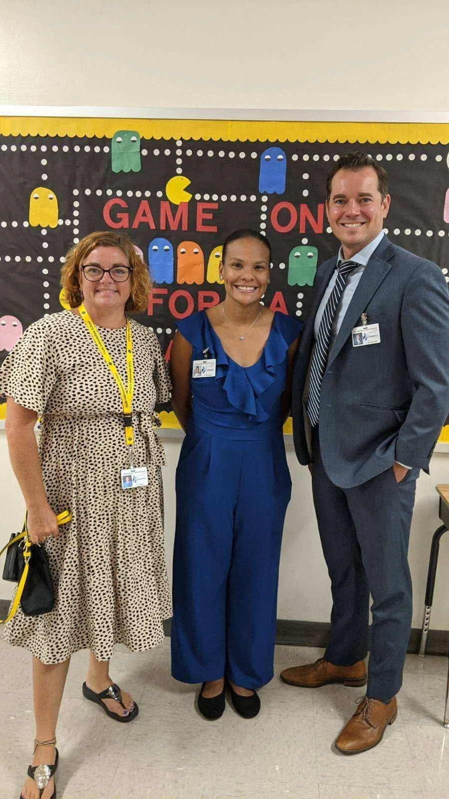 Three teachers standing in front of a classroom board with Pac-Man themed decorations, smiling at the camera.