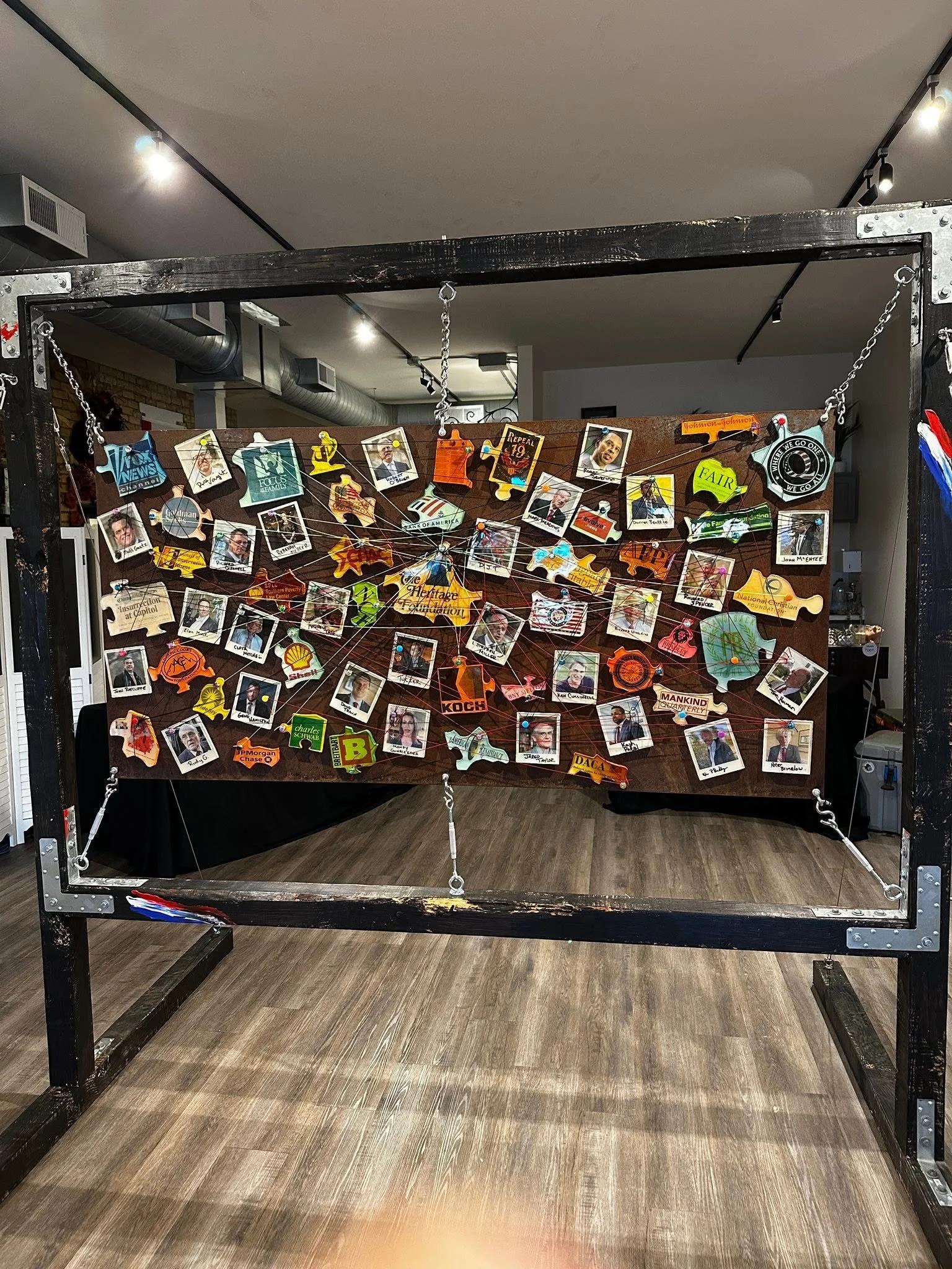 Installation view of Drew Wiggins’s “Exhibit A: Intentional Malfeasance,” showing a suspended steel frame filled with dozens of colorful fragmented images and materials connected across a dark backing.