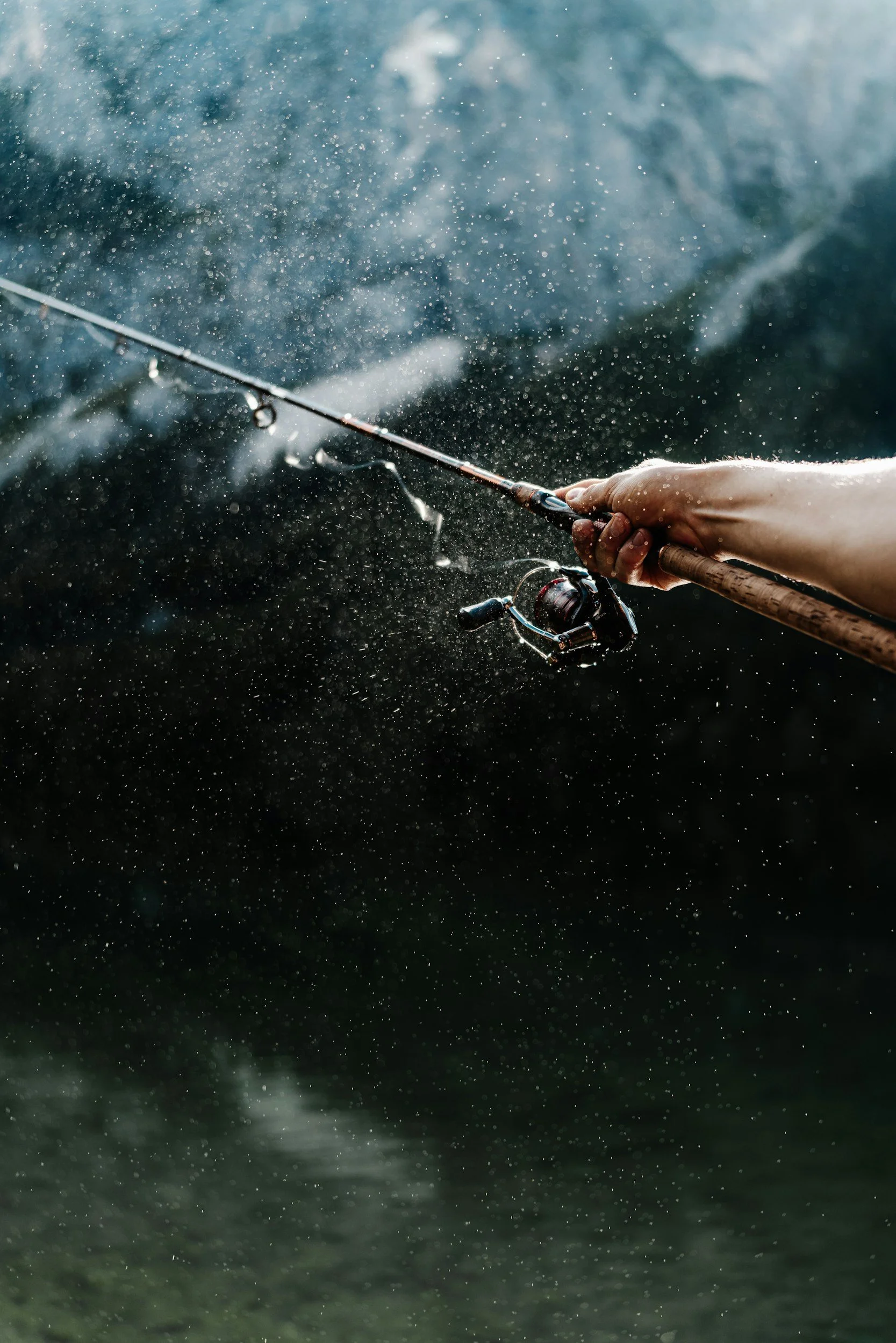 Close-up of a person holding a fishing rod with a baited hook in water, with water splash and droplets around.