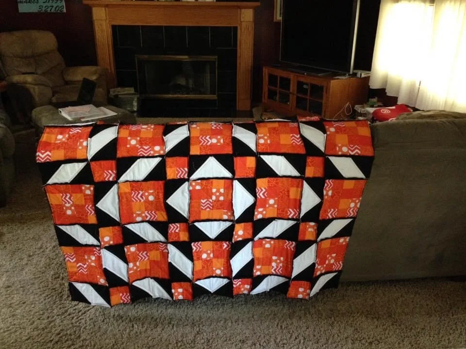 A colorful quilt with geometric patterns in black, white and orange.