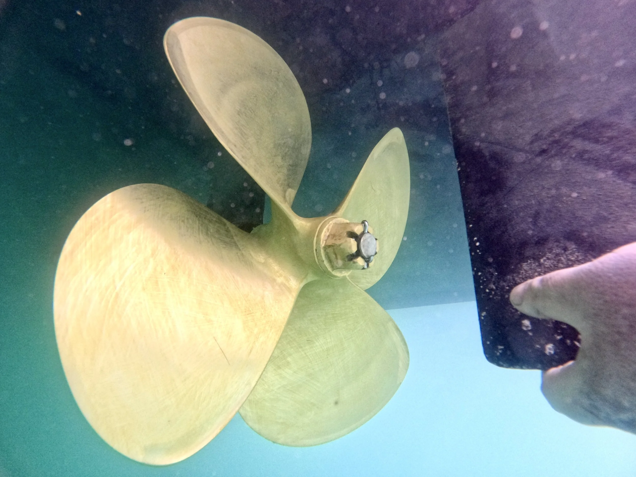 Close-up of a yellow submarine propeller underwater with dark purple and blue water around it.
