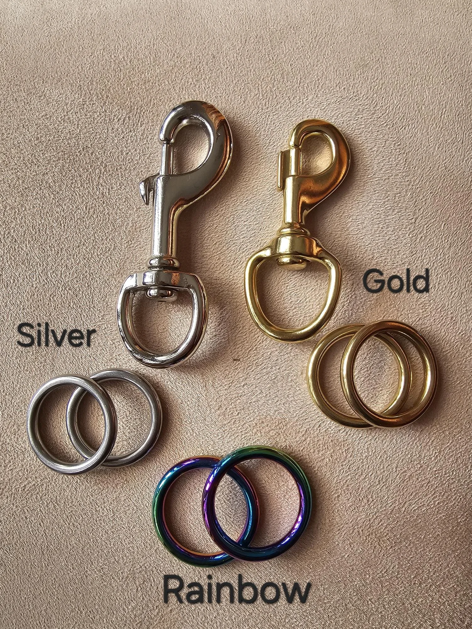 Close-up of colorful metal clasp hooks labeled with colors: silver, gold, rainbow, against a pink background.