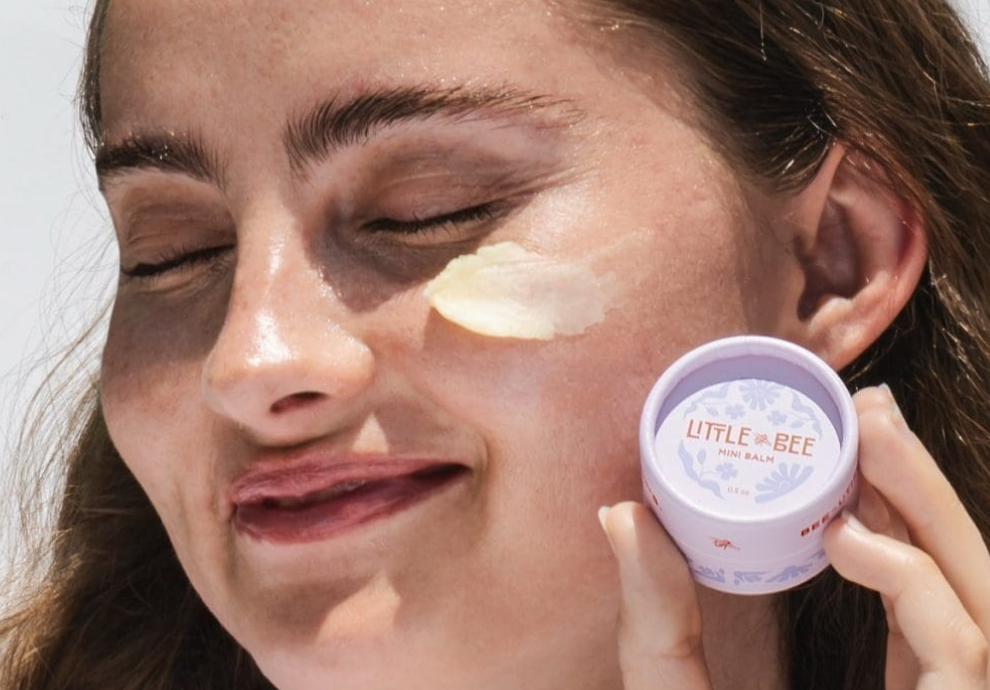Woman holding Little Bee mini balm with product applied to face