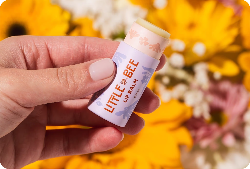 Woman holding Little Bee lip balm over a bed of flowers