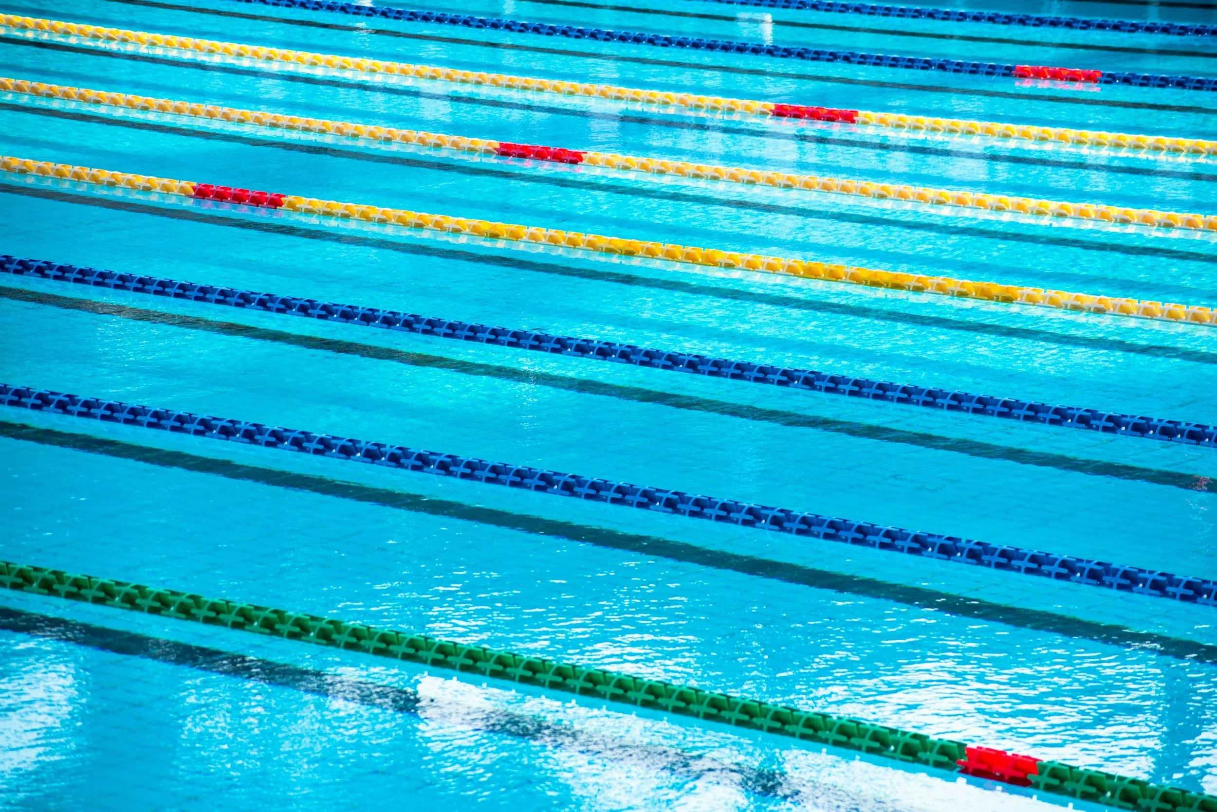 Multiple empty swimming pool lanes with lane dividers in yellow, red, blue, and green.