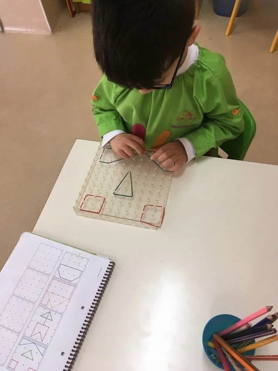 Criança brincando com um jogo de encaixe de formas geométricas em uma mesa de escola.