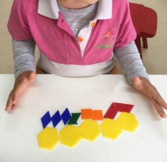 Pessoa com camiseta rosa e cinza, com objetos coloridos em formato de letras e hexágonos em uma mesa