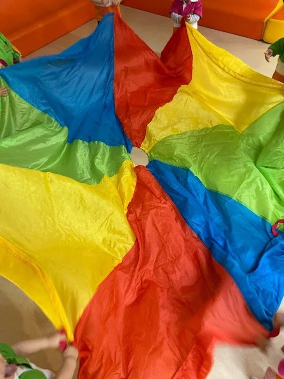 Crianças brincando com um parque de diversão feito de tecido com cores azul, vermelho, amarelo e verde.