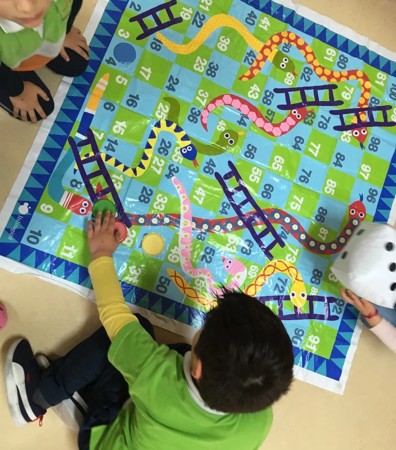 Crianças jogando um jogo de caça palavras de tabuleiro com uma pista de percurso de serpentes coloridas em um tabuleiro de plástico, com sãos de diferentes cores e uma peça de fichas.