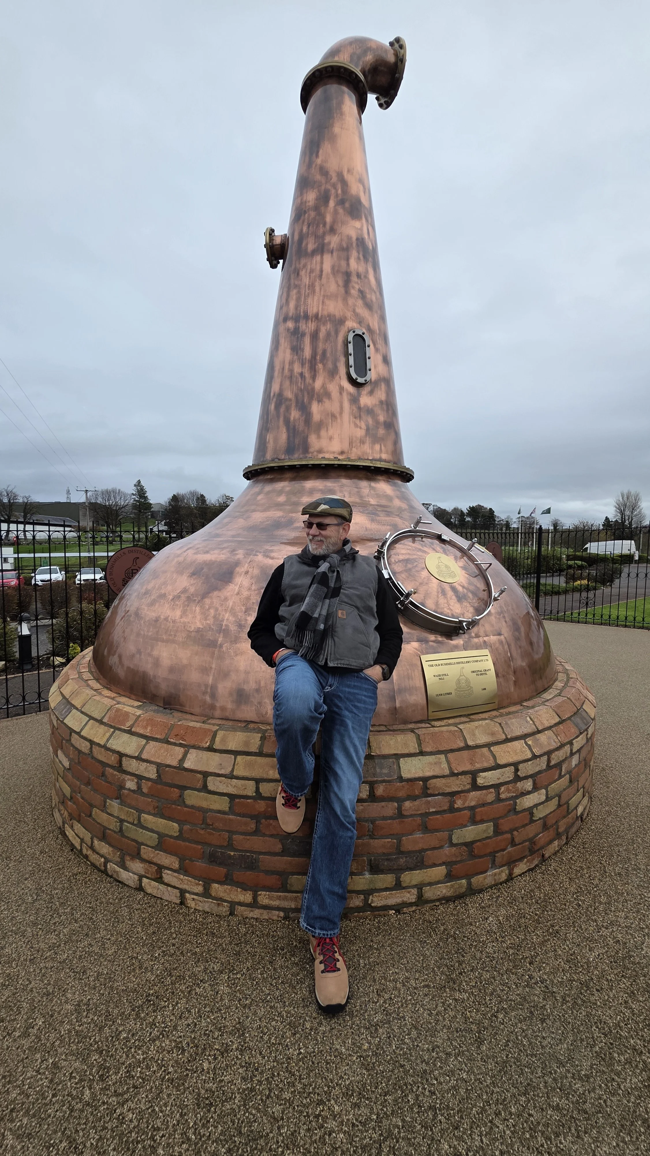 Darren Hudema leaning against a copper whiskey still outside Bushmills Distillery in Northern Ireland.
