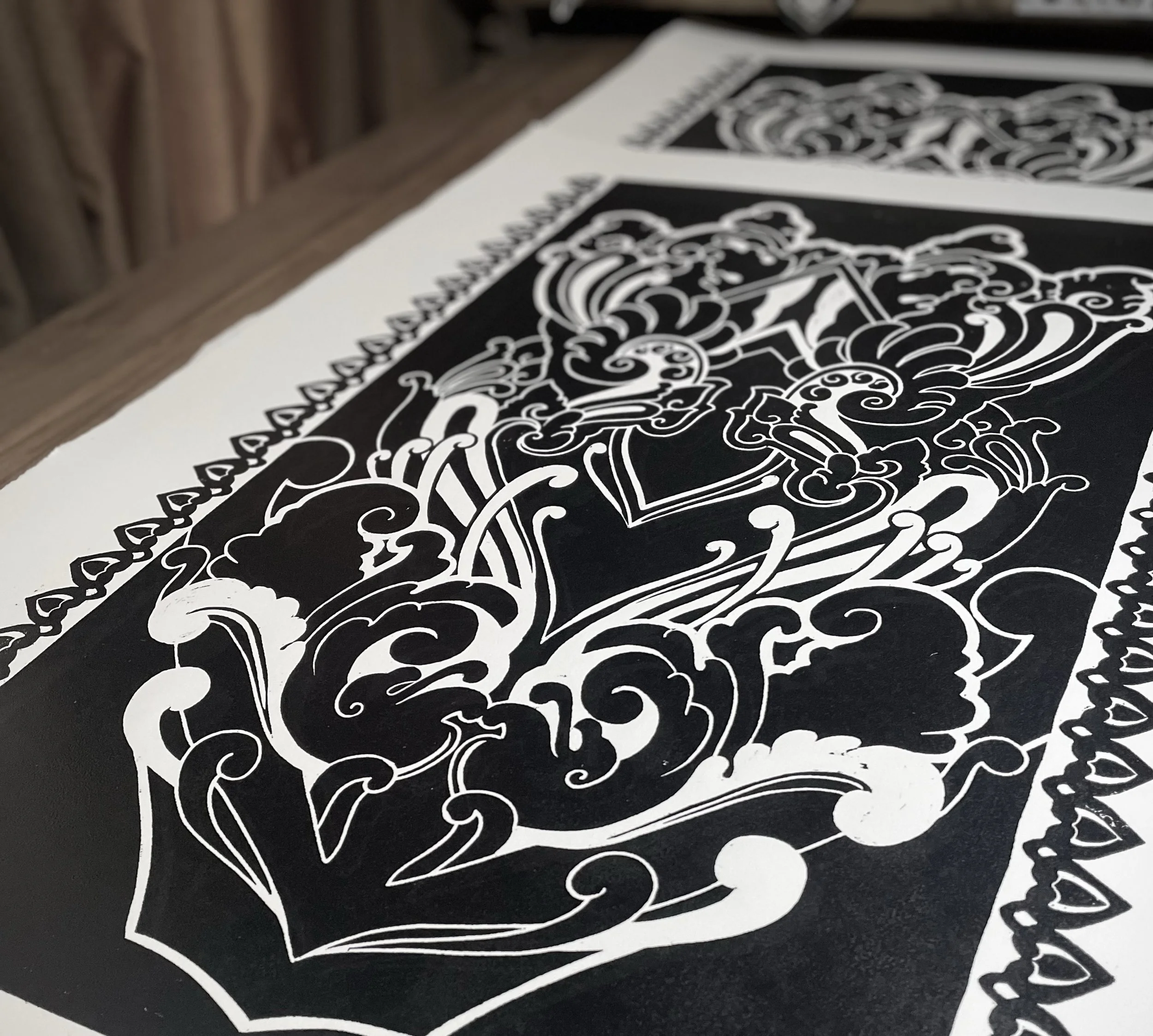 Close-up of a black and white ornate, detailed graphic or print design on paper, with intricate swirling patterns and symmetrical motifs.