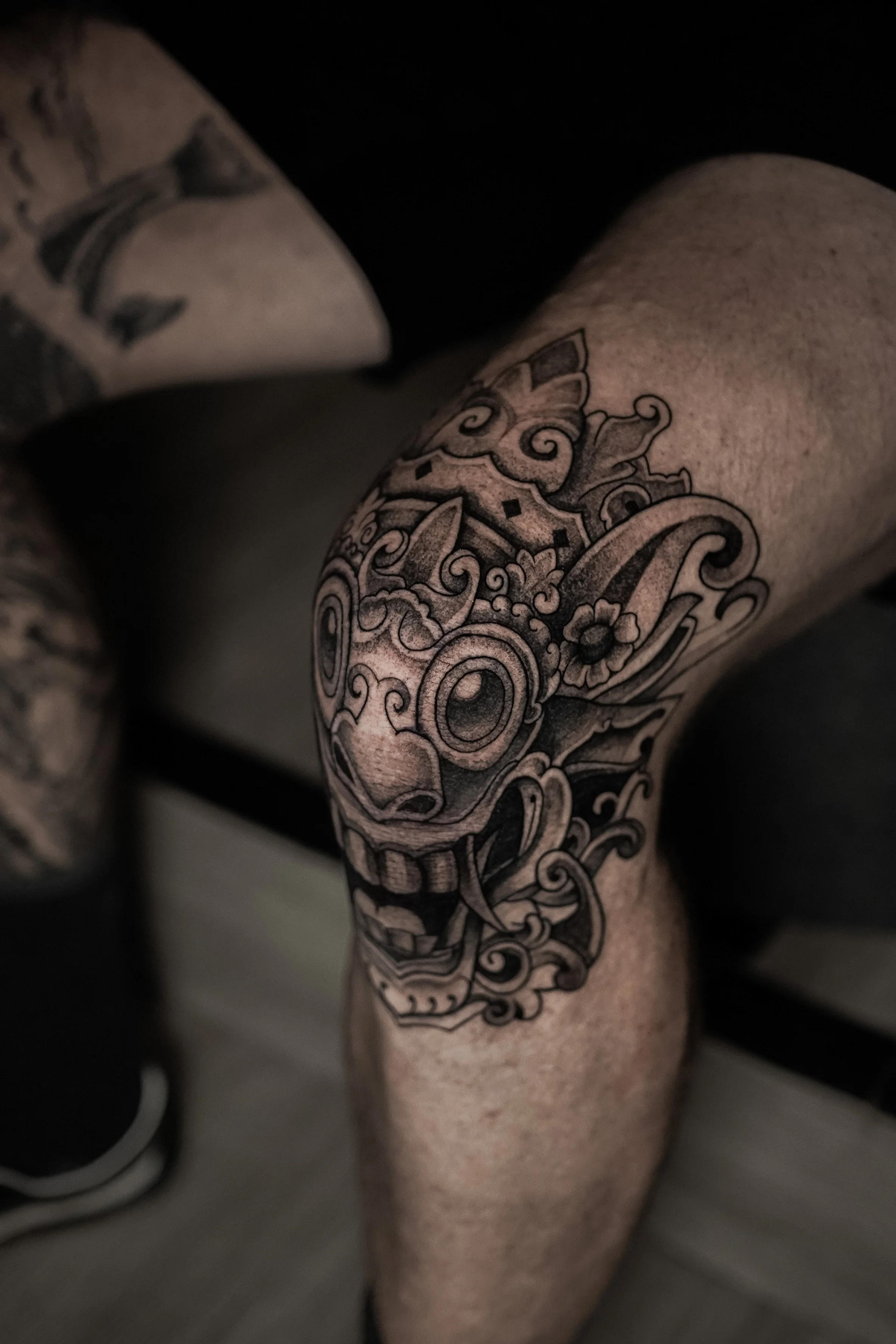 Close-up of a person's arm showing a large, intricate black tattoo with floral and swirling designs.