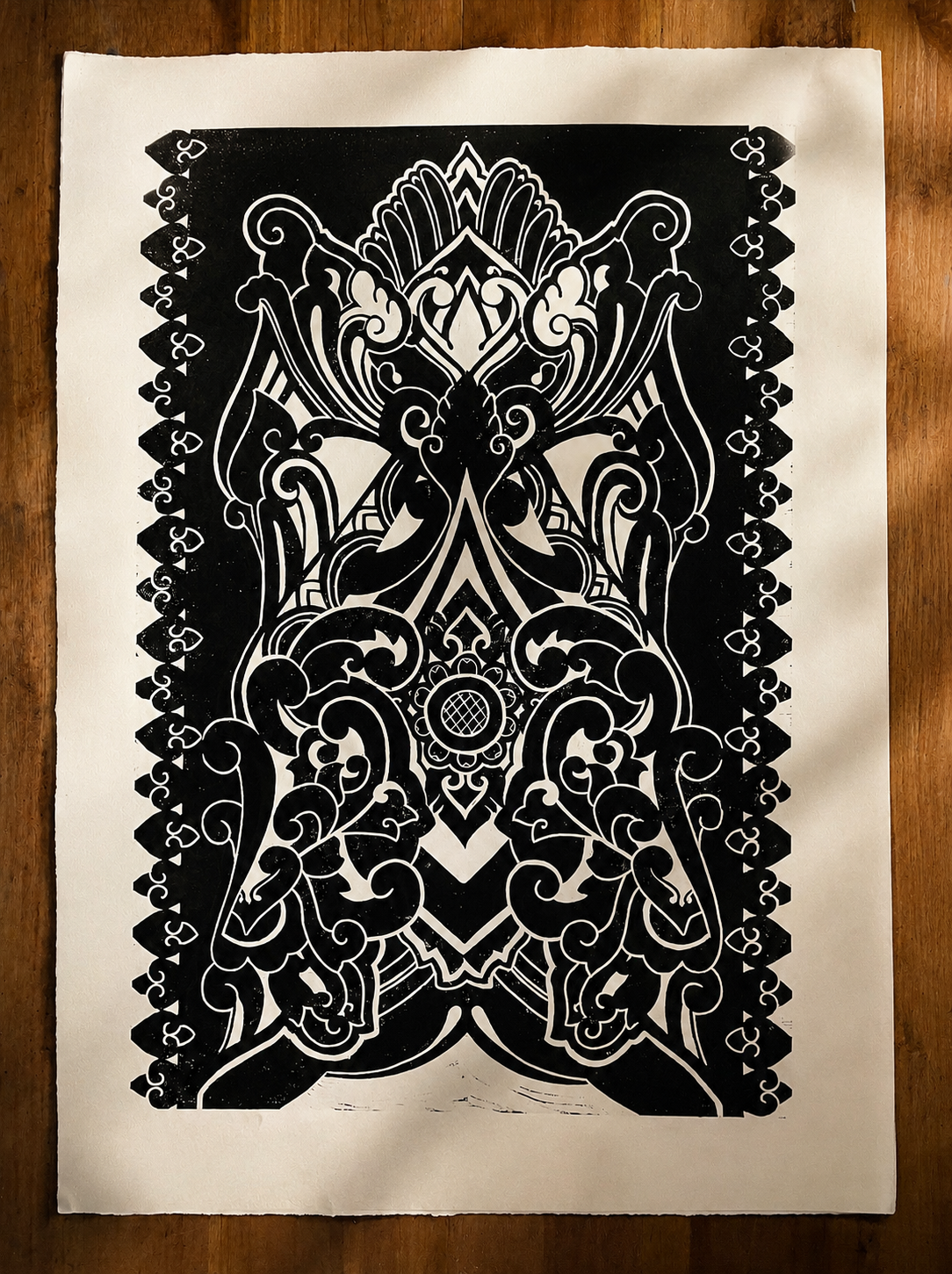 A black and white intricate, symmetrical paper cut-out design on beige paper, featuring swirling patterns, floral elements, and ornate details.