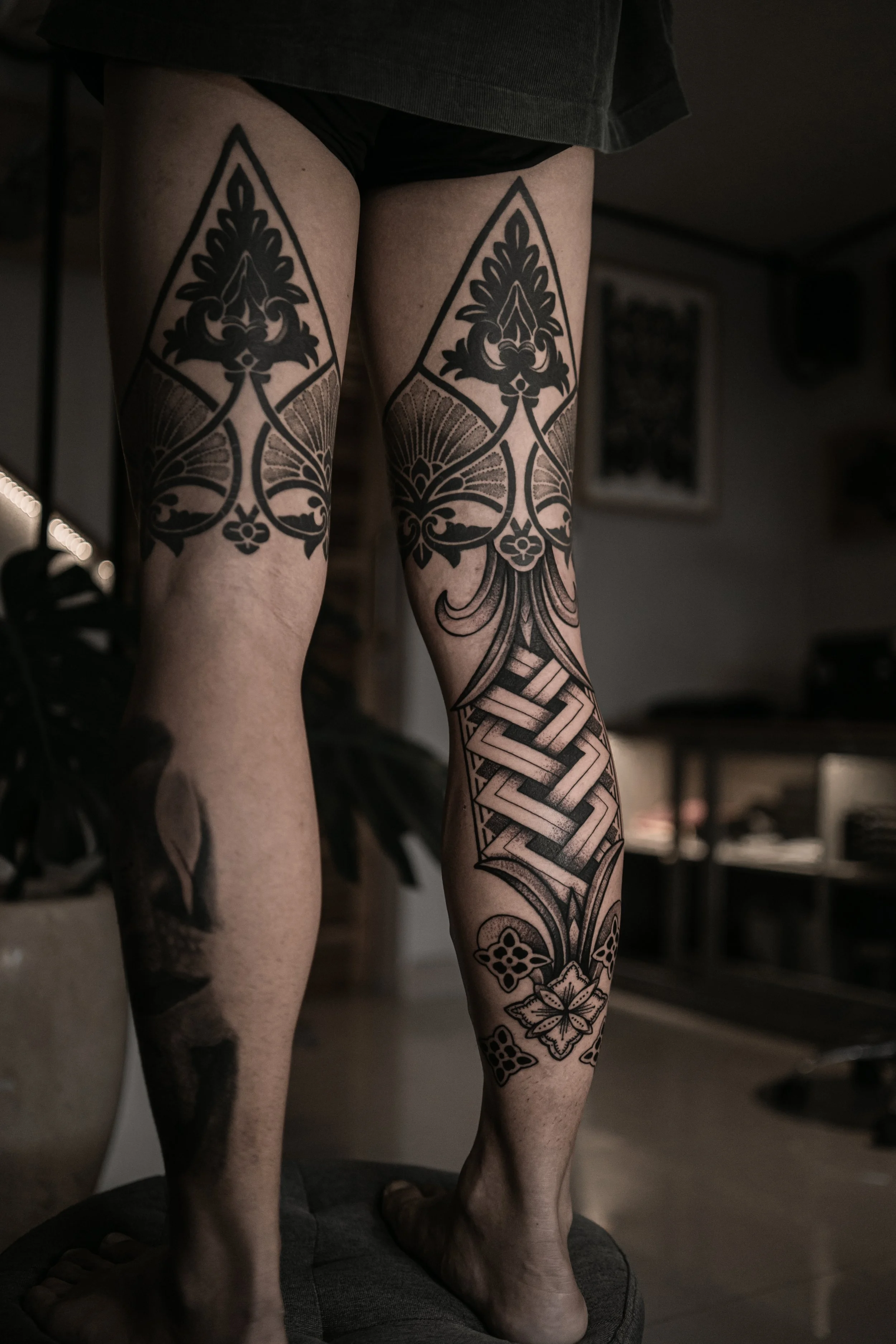 Close-up of tattooed legs on a statue, featuring intricate black designs including floral patterns and geometric shapes.