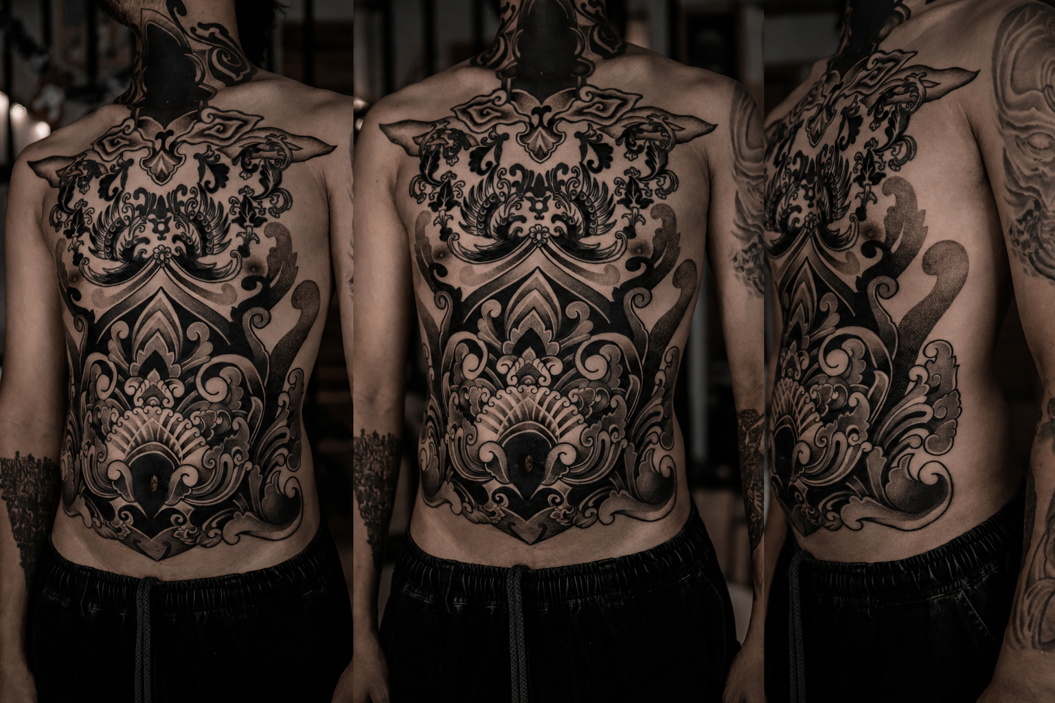 Person with extensive black tattoo sleeve on left arm and chest, and large intricate black tattoo across chest and stomach, standing shirtless in a dark setting.