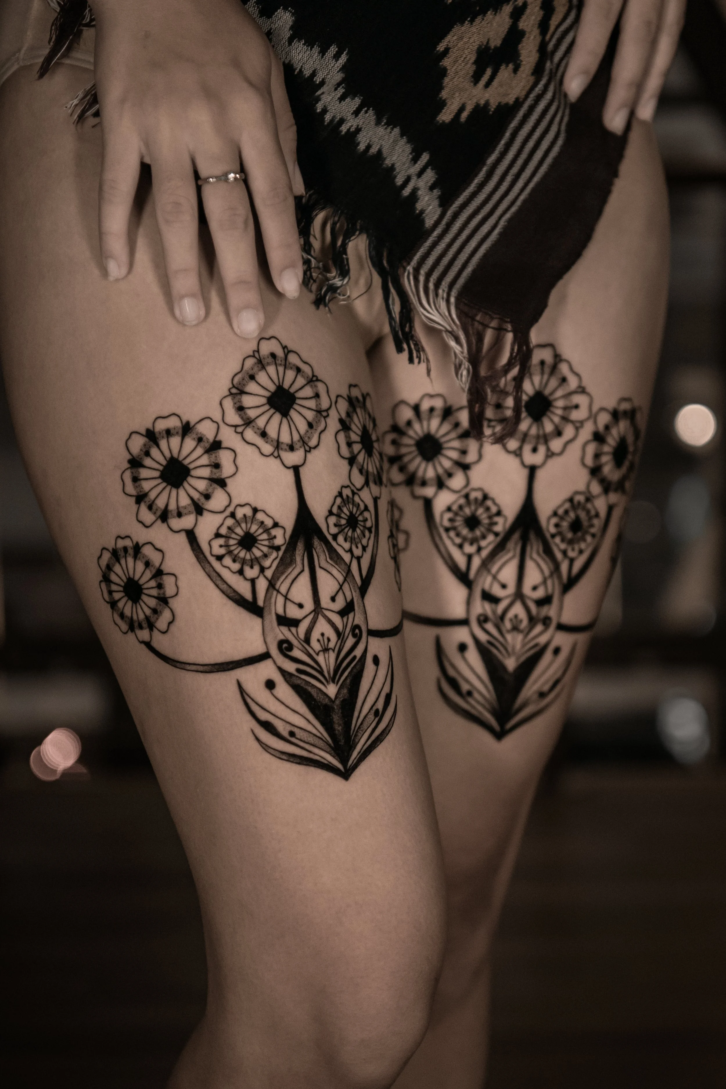 Close-up of a person wearing a patterned shawl or blanket and decorated with intricate black floral tattoos on their thighs.