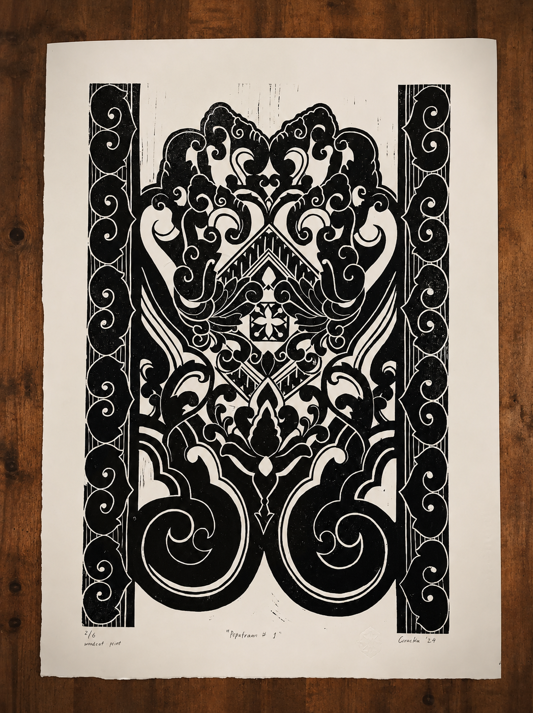 Black and white woodcut print titled 'Paparann #1' featuring intricate, symmetrical, floral and abstract patterns, signed by the artist Greehyde in 2024, numbered 2/6, on a white paper with wooden surface background.