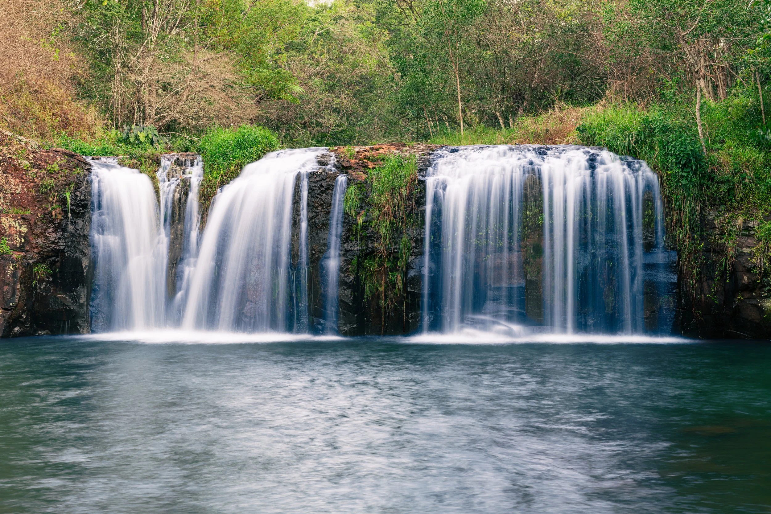 A waterfall flowing over rocks surrounded by lush greenery and trees.