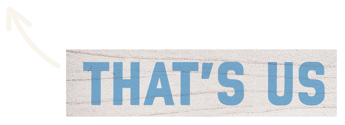 Close-up of a sign with the words 'THAT'S US' written in large blue letters on a light wooden background.