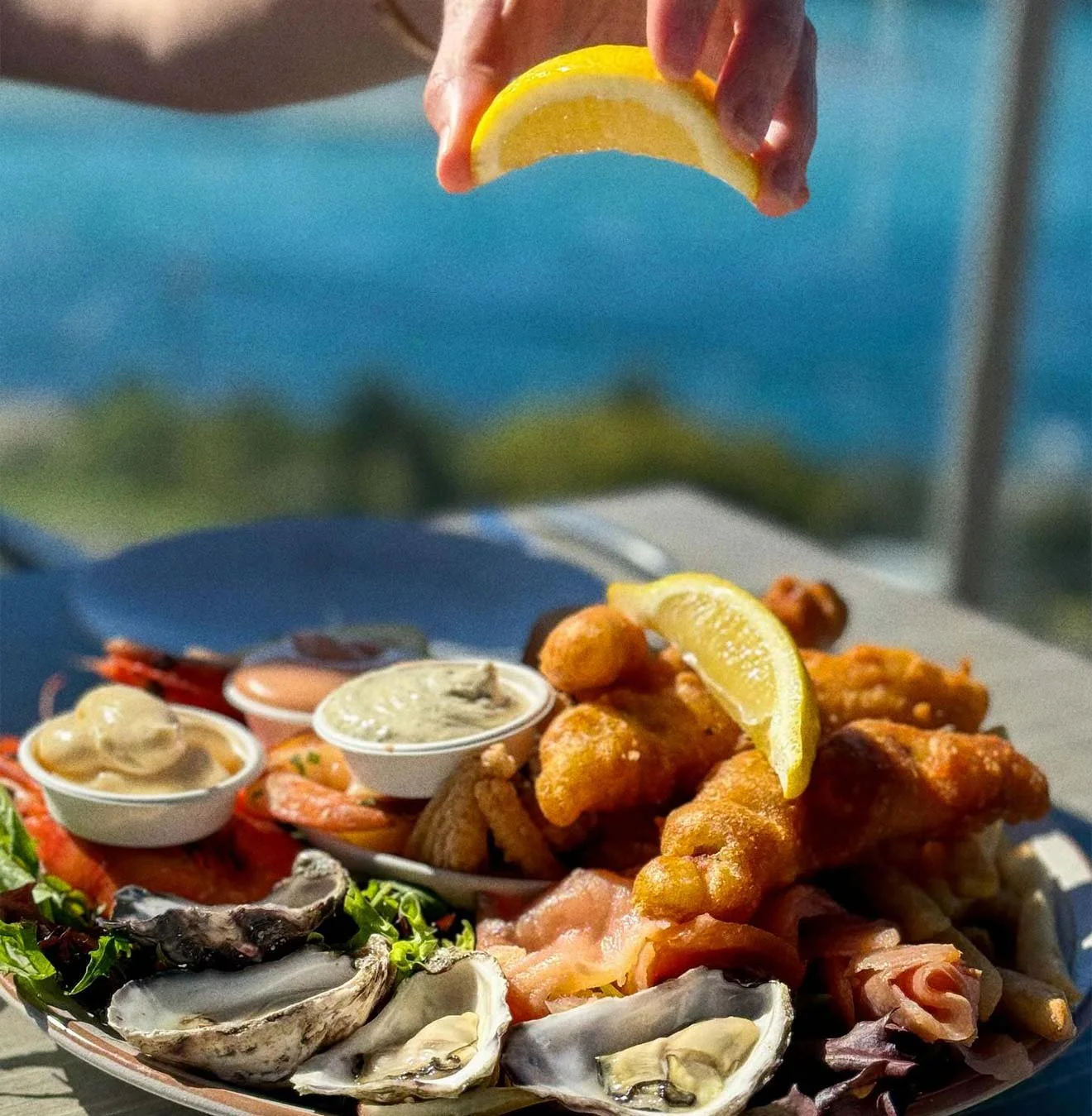 A tray of assorted seafood including oysters, fried fish, and shrimp, garnished with lemon slices, with various dipping sauces.