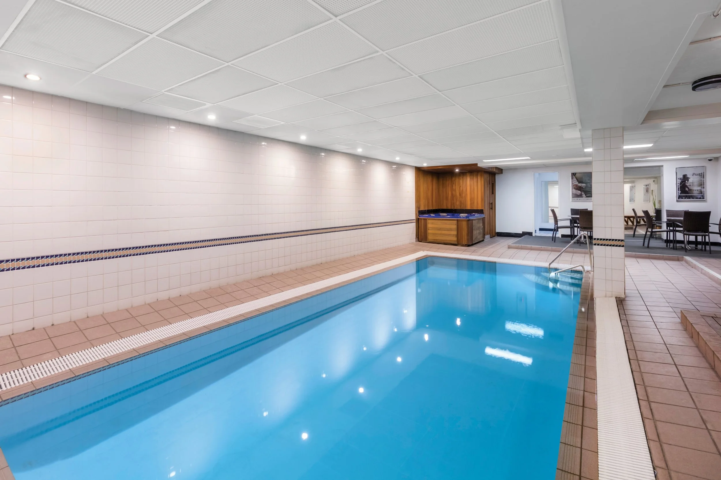 Indoor swimming pool with tiled floor and walls, with lounge chairs and framed pictures on the walls.