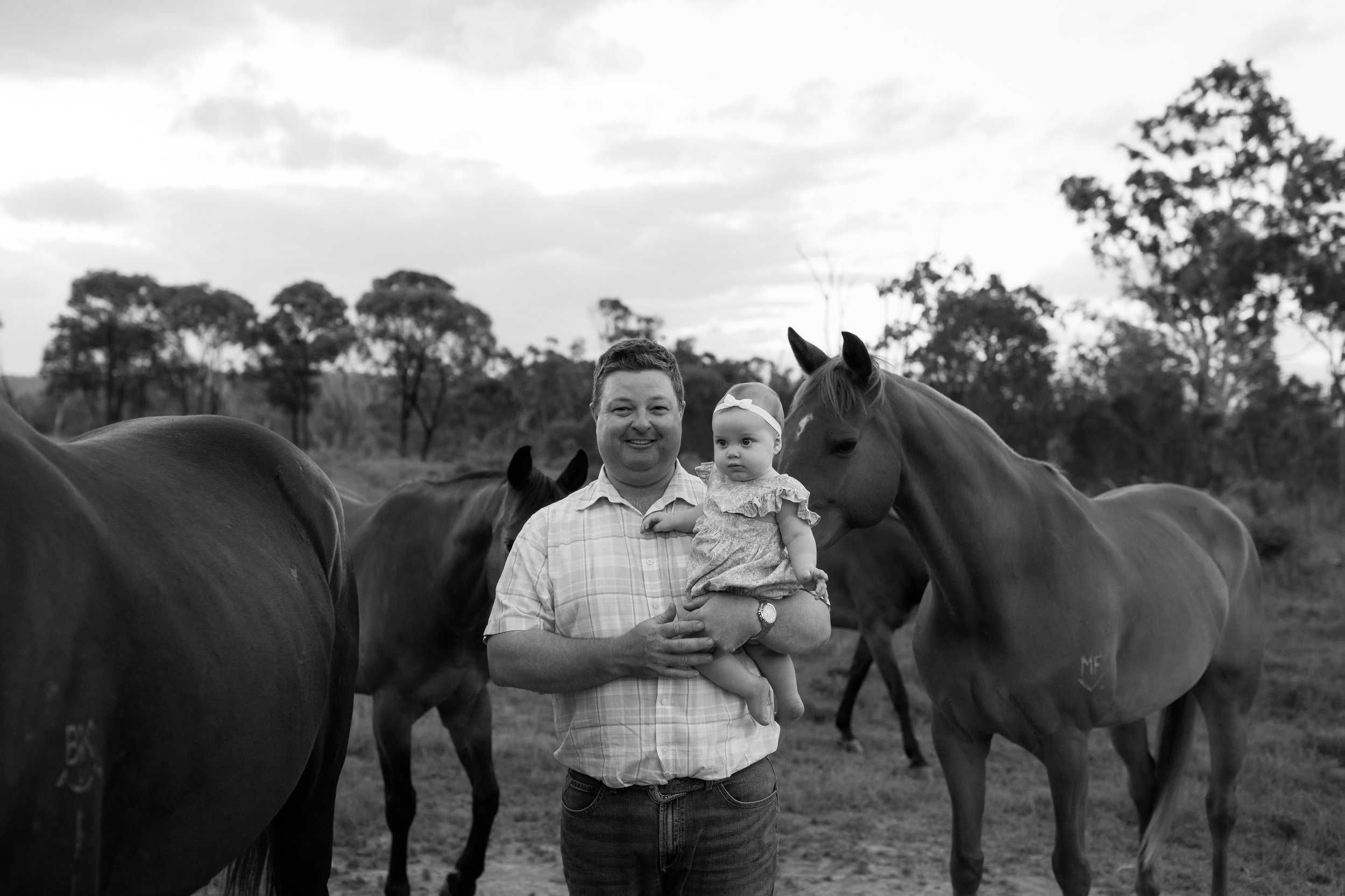A man holding a young girl in front of horses outdoors on a cloudy day.